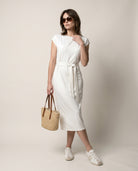 Woman wearing a white dress holding a woven bag against a plain background