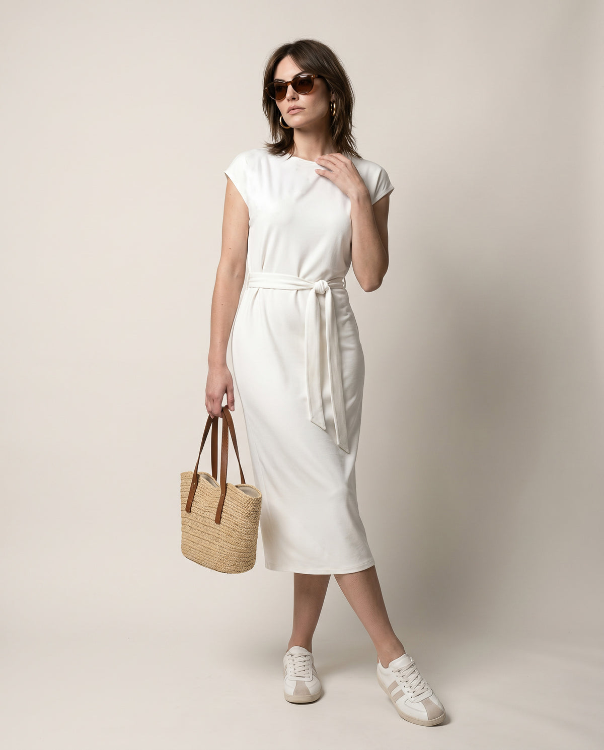 Woman wearing a white dress holding a woven bag against a plain background